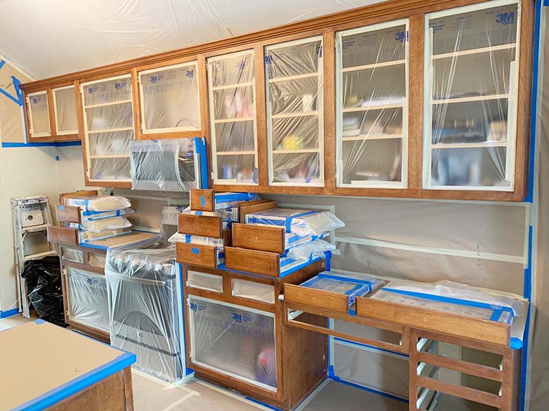 Kitchen with cabinet doors removed, insides masked for painting