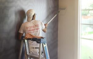 painter-rolling-paint-and-primer-in-one-on-wall-next-to-wallpaper